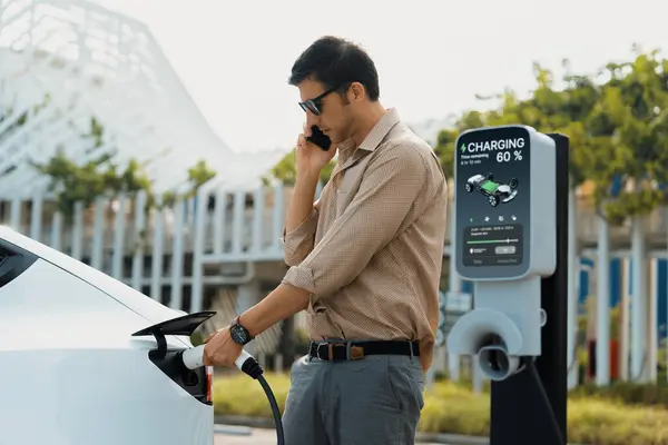Driver charging electric vehicle at charging station